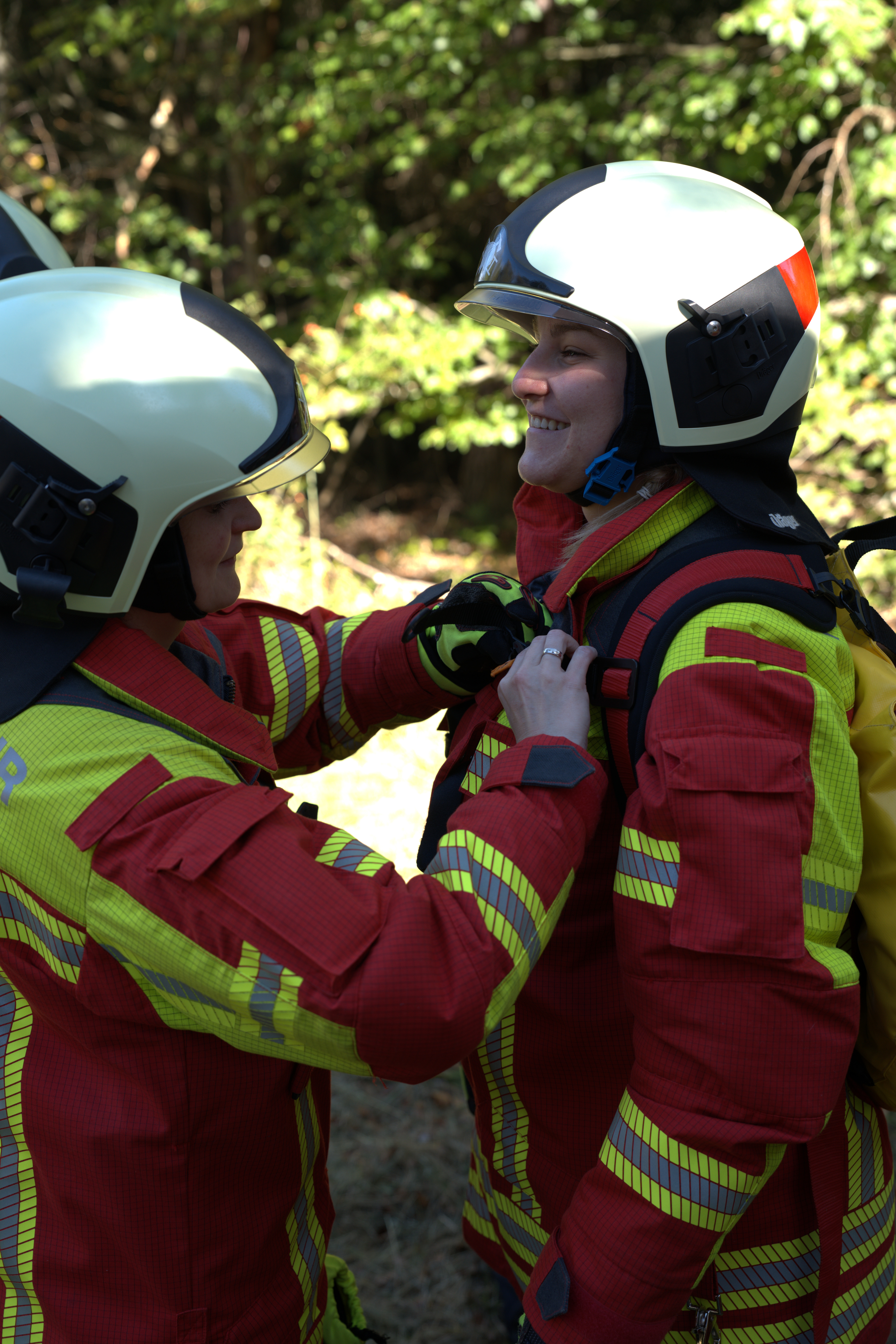 Zwei Feuerwehrfrauen in Uniform helfen sich bei der Kleidung.