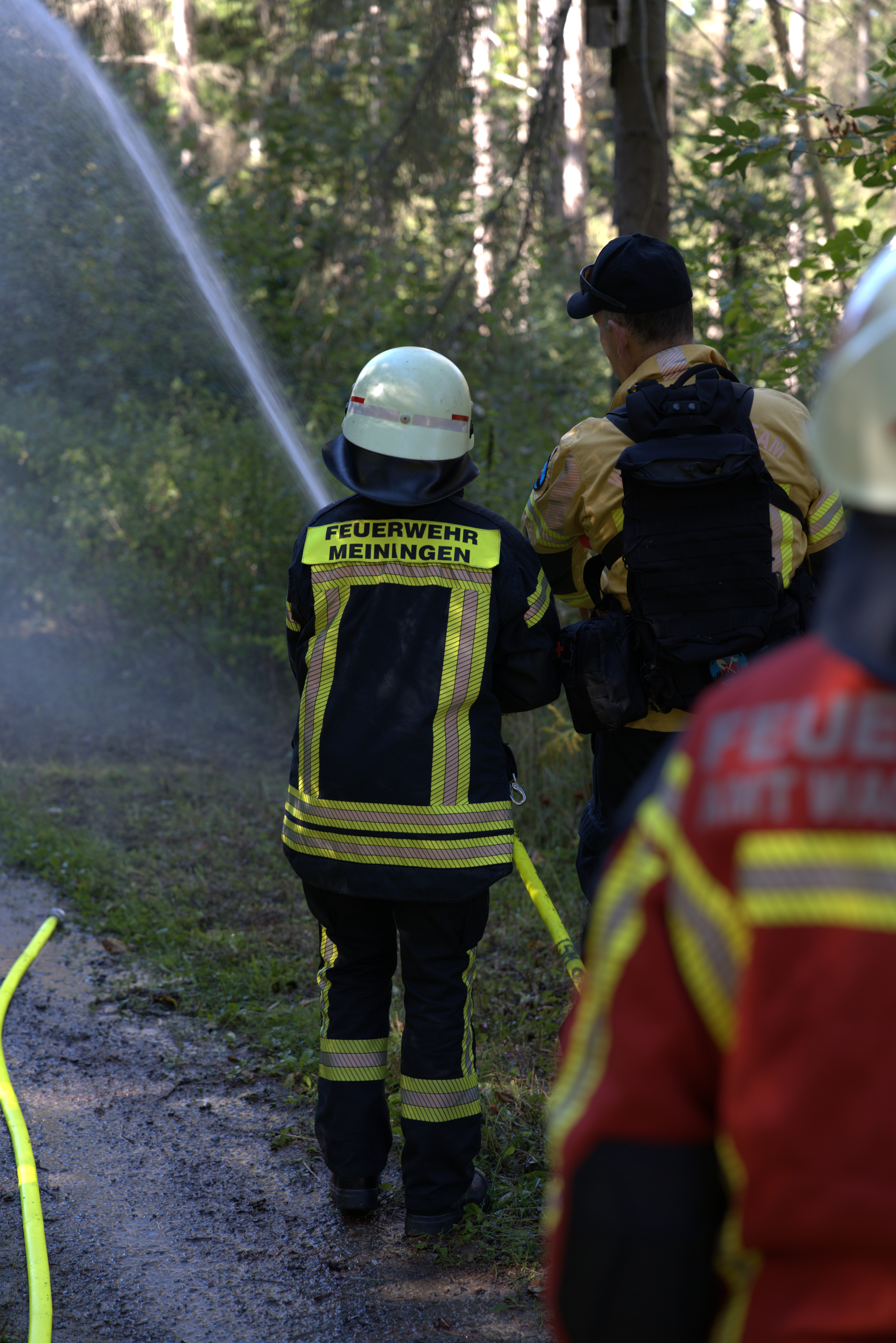 Eine Feuerwehrfrau in Uniform von hinten spritzt Wasser aus dem Bild heraus.