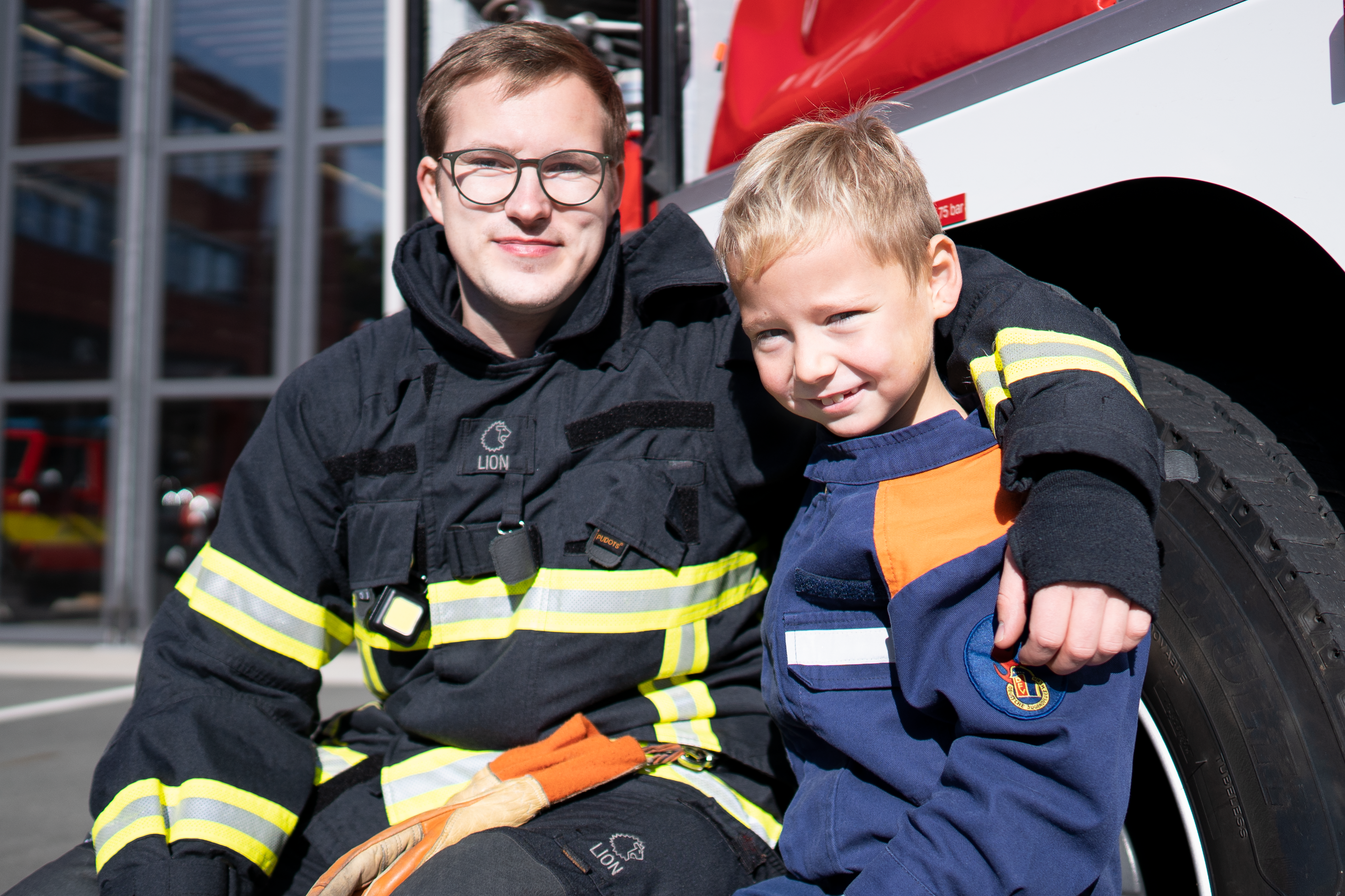 Ein Feuerwehrmann in Uniform und ein Kind der Jugendfeuerwehr