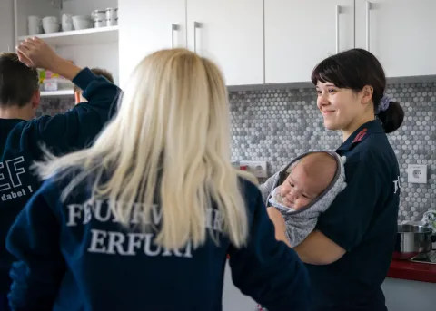 Zwei Feuerwehrfrauen mit Kind im Arm.