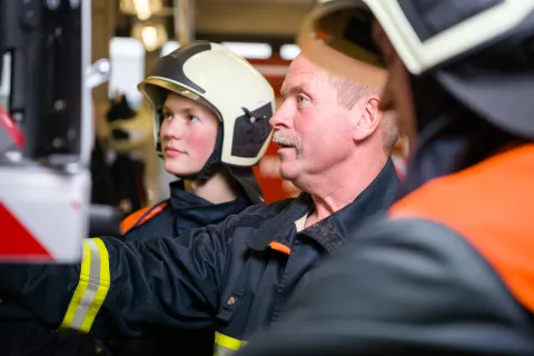 ein junger und ein erfahrener Feuerwehrmann am Feuerwehrfahrzeug