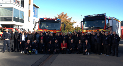 Gruppe von Feuerwehrmenschen in Uniform vor zwei Feuerwehrautos