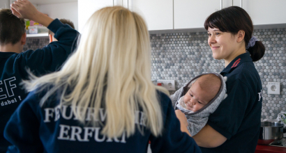 Zwei Feuerwehrfrauen mit Kind im Arm.