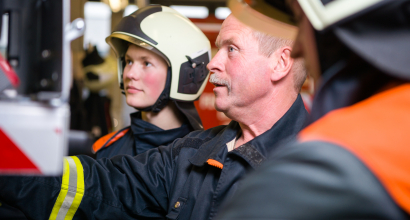 ein junger und ein erfahrener Feuerwehrmann am Feuerwehrfahrzeug